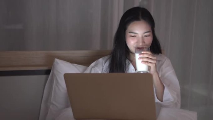 女人使用笔记本电脑，微笑着喝牛奶
