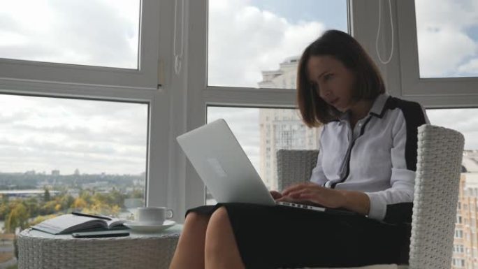 年轻专注的女商人穿着严格的衣服坐在现代办公室里，拿着笔记本电脑，等待答案，对失去与合作伙伴的交易感到