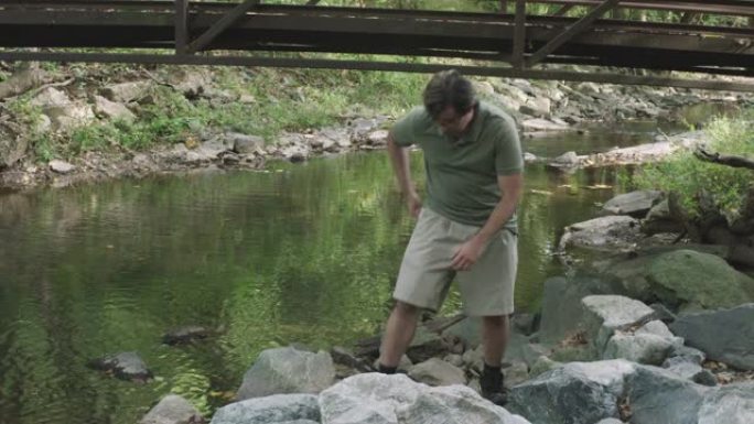 一名男子从桥上跑到一条小溪上，从水中拔出手机。