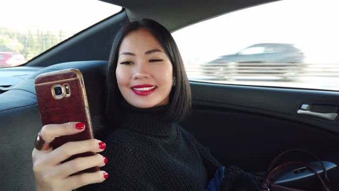 坐在后座上的亚洲妇女在汽车上使用手机