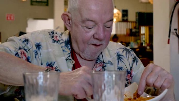 饥饿的老人独自在餐厅里用叉子吃意大利面