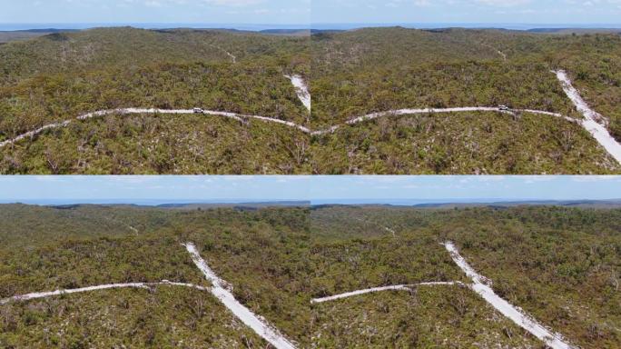 美丽的空中高角度无人机视图，四轮驱动越野车在澳大利亚昆士兰州弗雷泽岛的内陆沙地道上驶过森林。