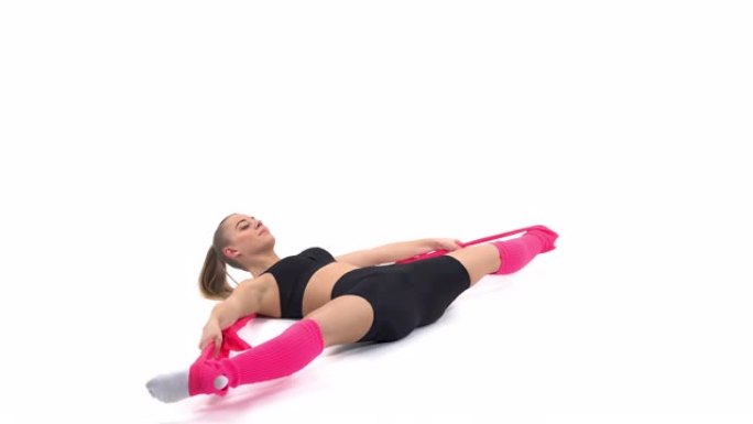 一名专业女运动员仰卧，用弹性绳进行伸展运动的侧视图。孤立，在白色背景上