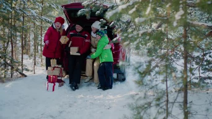幸福的家庭在冬季森林的汽车后备箱中寻找新年礼物。妈妈、爸爸、儿子和女儿戴着红色圣诞帽，寒假时在白雪皑