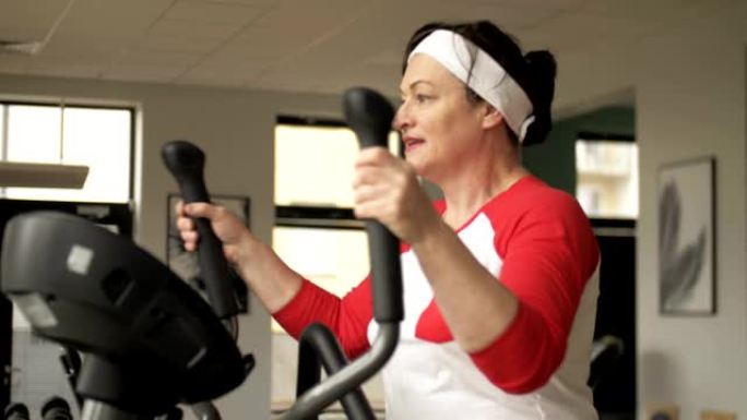 迷人的白人女性在训练机上锻炼身体，在健身中心看起来很开心。中年时期的健身和积极运动