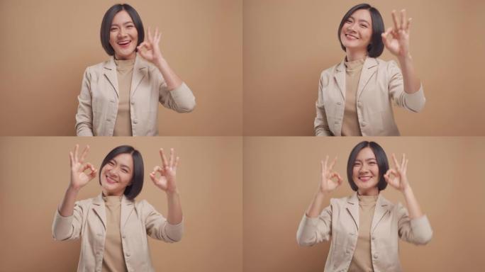 亚洲女商人快乐的微笑展示她的手在米色背景上孤立的OK手语。4k视频