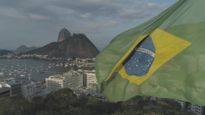 一架无人机被拍到飞过飘扬在阳光下的巴西国旗，上面显示着甜面包山里约热内卢de Janeiro
