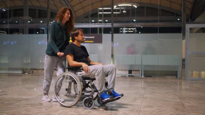 快乐残疾男子坐轮椅与快乐年轻女子在机场跑步