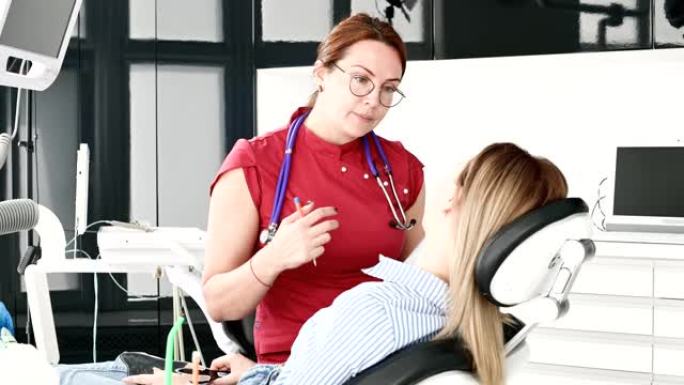 一名年轻女孩正在与一名戴着眼镜的牙医妇女进行咨询，正坐在一间诊所的椅子上。医生和病人的谈话