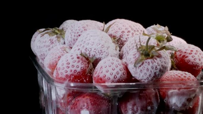 黑色背景的一次性塑料食品包中的新鲜冷冻草莓。旋转360度，特写