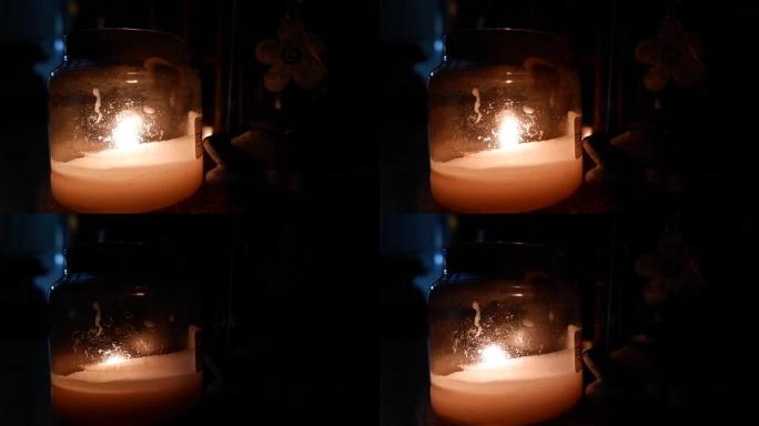 蜡烛在黑暗背景的桌子上的玻璃杯中燃烧。