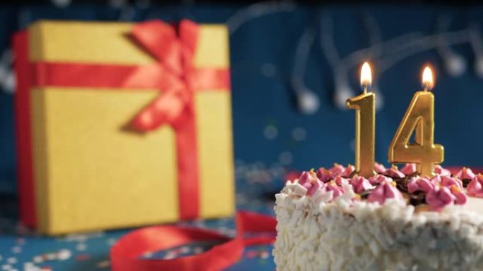 白色生日蛋糕编号14点灯燃烧的金色蜡烛，带灯的蓝色背景和用红丝带绑起来的礼物黄色盒子。特写