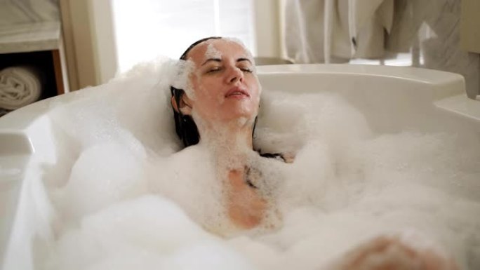 快乐的女人享受充满泡沫的沐浴。美女在家享受水疗