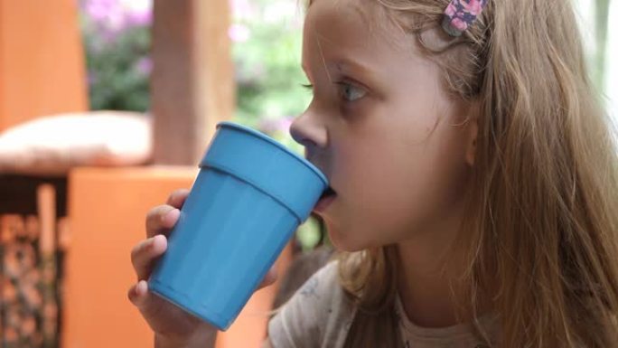 可爱的孩子用蓝色塑料玻璃喝水