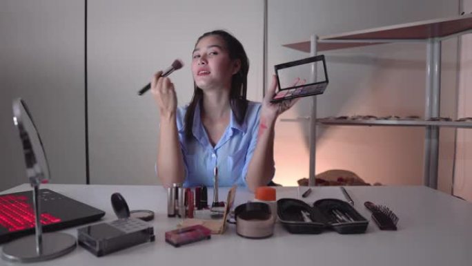年轻迷人的亚洲女性博客作者或视频博客作者看着相机，晚上谈论卖化妆品