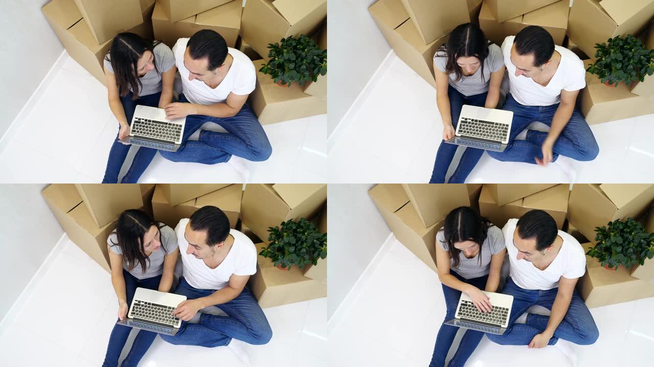 夫妇坐在新公寓的地板上，在笔记本电脑上进行在线购物，选择家具和装饰元素。
