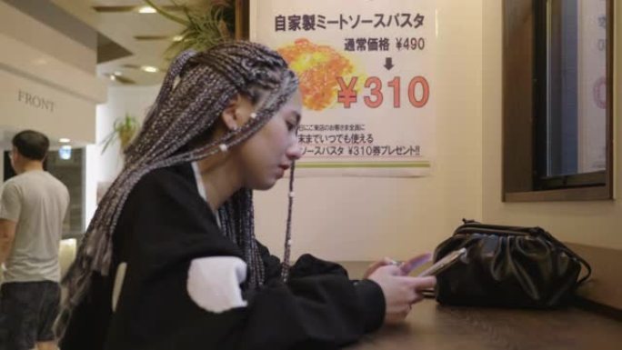 年轻的亚洲妇女在餐厅检查智能手机