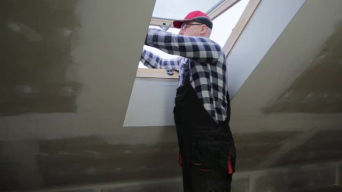 杂工，建筑工人在新的隔热和填充的干墙阁楼中安装PVC窗户。