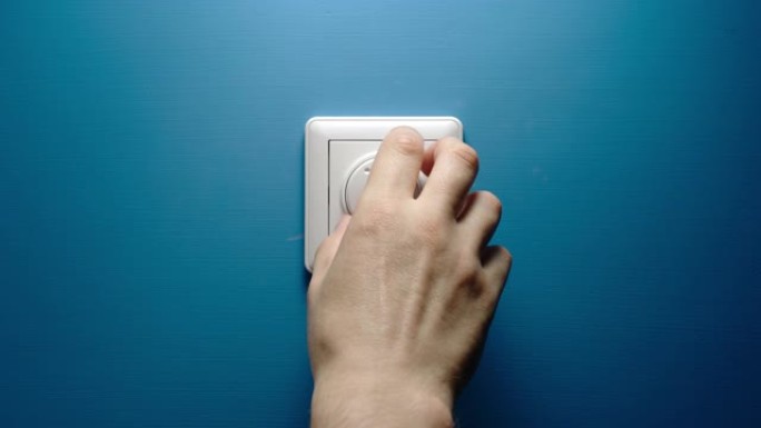 人的手慢慢地转动蓝色墙壁上的调光按钮