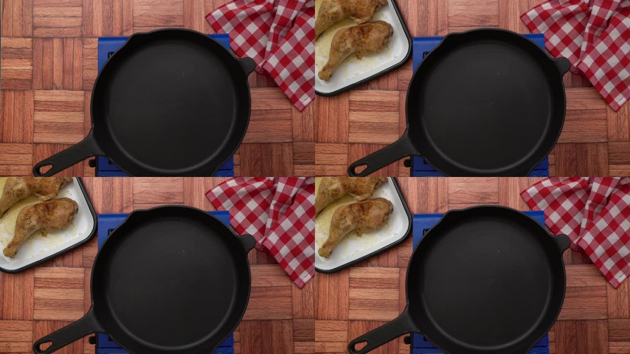 女主厨正把一盘炸鸡腿放在火炉上的空铁铸盘旁，顶视图