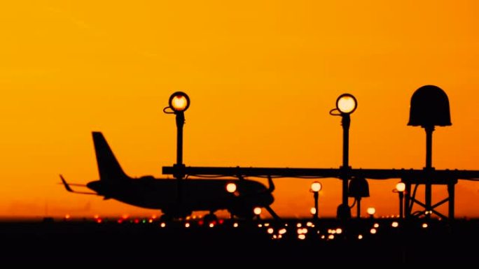 在阳光明媚的橙色和紫色日落时，机场的飞机轮廓。飞机在跑道上滑行，为旅行做准备。跑道末端识别灯和频闪发