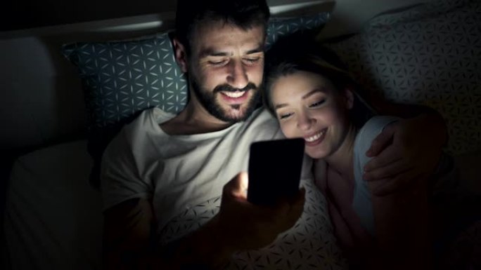 可爱的情侣躺在床上看手机好玩的东西