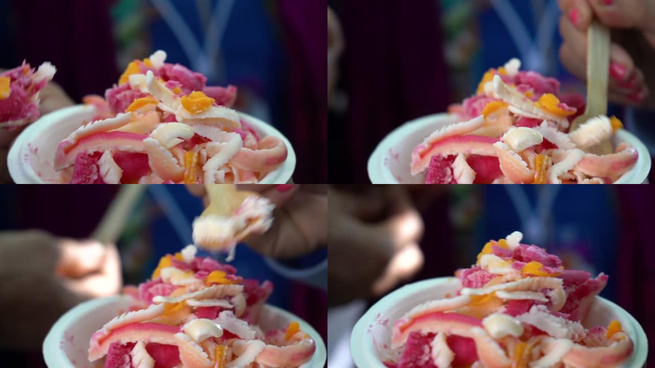 人们在一次性纸盘上用木勺从冷冻圆筒滚筒上刮牛奶，味道和颜色制成的冰淇淋