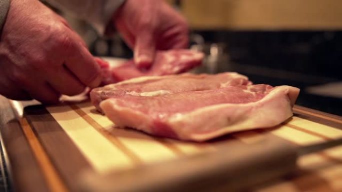 在准备烧烤的木制切菜板上放下新鲜未煮过的生去骨里脊肉猪排的慢动作镜头