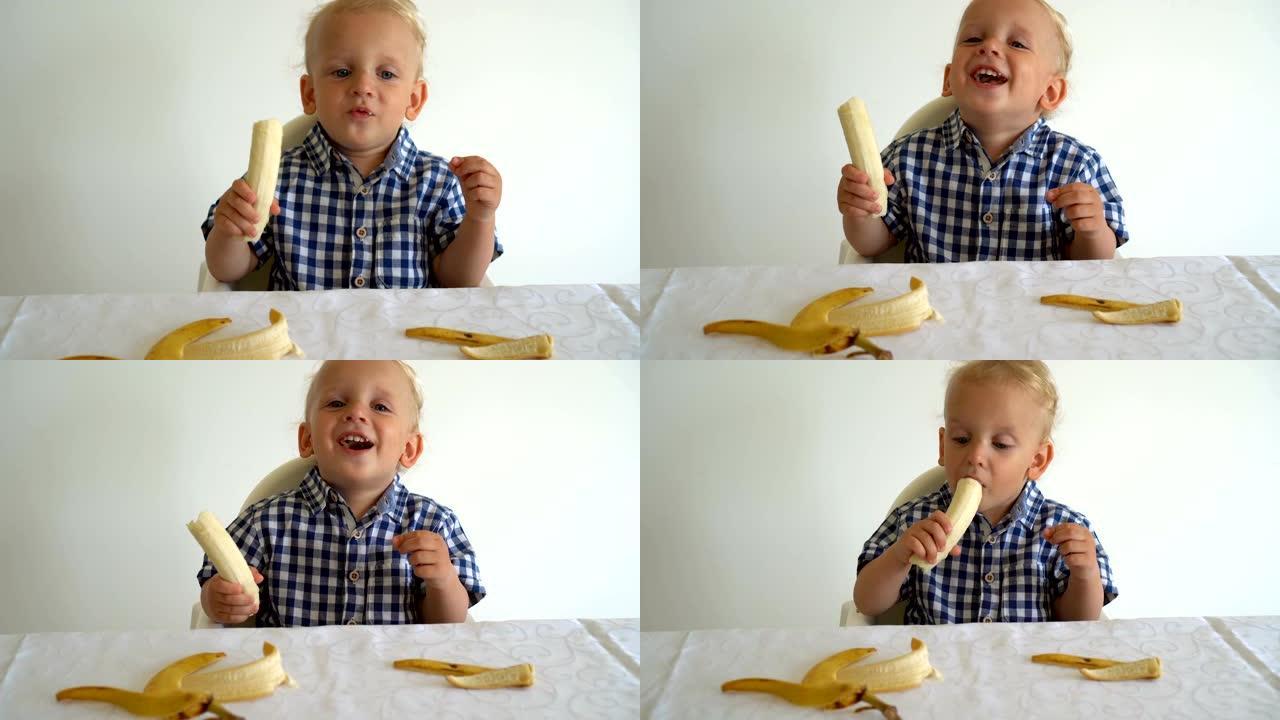 无辜的脸孩子吃香蕉坐在白色背景的桌子旁边。万向节运动