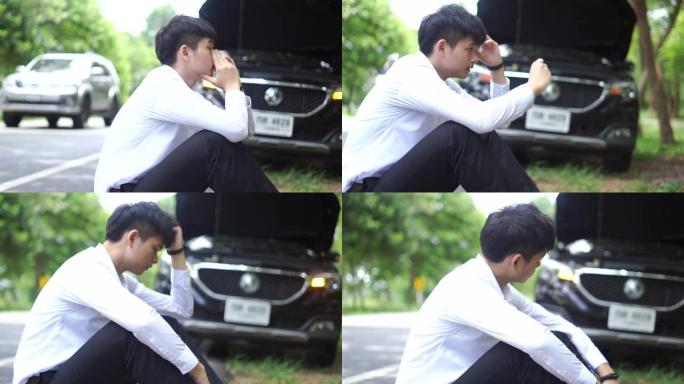 一名年轻的亚洲男子坐在路边一辆破车前