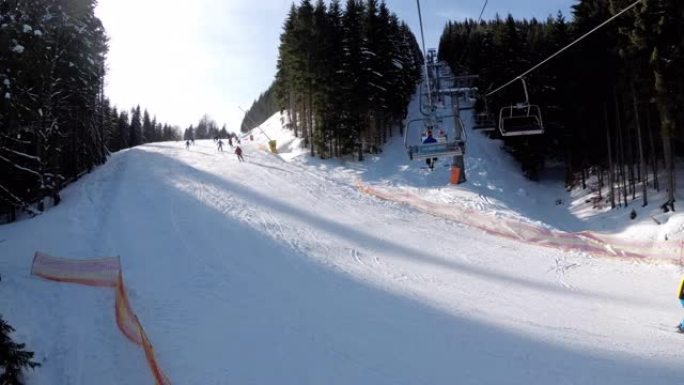 POV从滑雪椅升降机到白雪皑皑的滑雪场，滑雪者在滑雪场上滑行。滑雪场