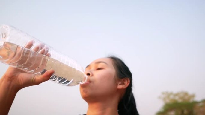 亚洲年轻女子在公园慢跑后用塑料瓶喝水。减肥。健康的生活方式理念。