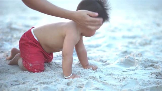 可爱的蹒跚学步的男孩在阳光明媚的夏日在沙滩上爬行。