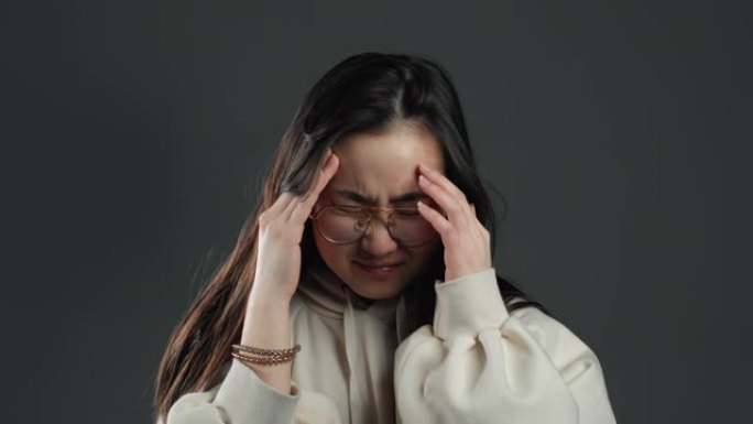 年轻的韩国亚洲女子长发头痛，工作室肖像。女孩把手放在头上，孤立在灰色背景上。问题和头痛的概念。