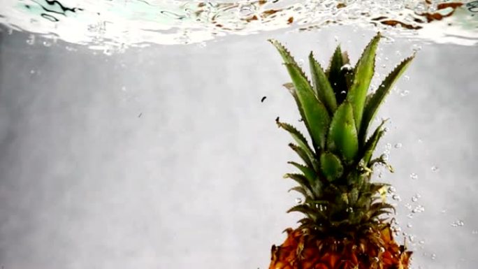 菠萝落入水中，有很多小气泡。孤立白色背景上的菠萝视频。