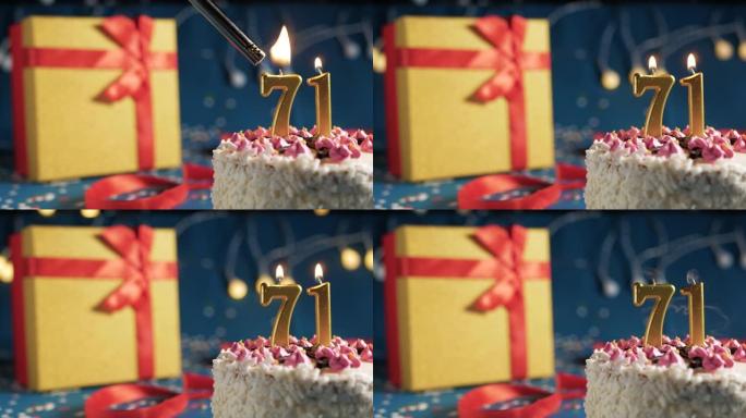 白色生日蛋糕编号71点灯燃烧的金色蜡烛，带灯的蓝色背景和用红丝带绑起来的礼物黄色盒子。特写