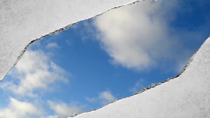 创造性的时间圈视频，在蓝天中快速移动的云，可以通过旧复古垃圾老式纸的边缘撕裂的孔看到。