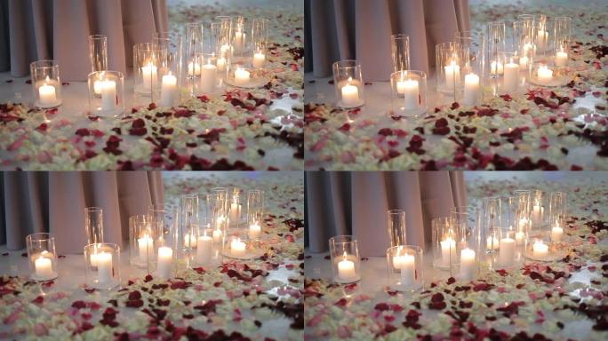 玻璃烧瓶中的白色燃烧蜡烛，玫瑰花瓣躺在冰上