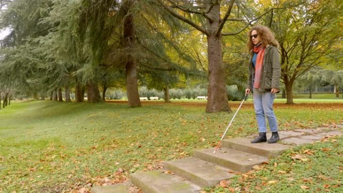 美丽的盲女人拄着白色手杖走下公园的台阶