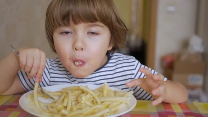 可爱的小男孩在厨房吃奶酪意大利面。肖像有趣的健康学龄前儿童男孩吃意大利面。饥饿的孩子用手吃饭，在家微