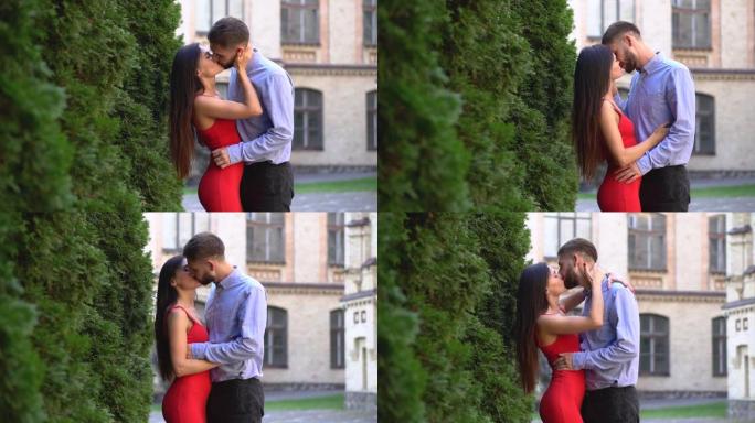 美丽的一对男女朋友在公园背景下散步和接吻。男人和女人爱。穿红色连衣裙的女孩和一个男人。