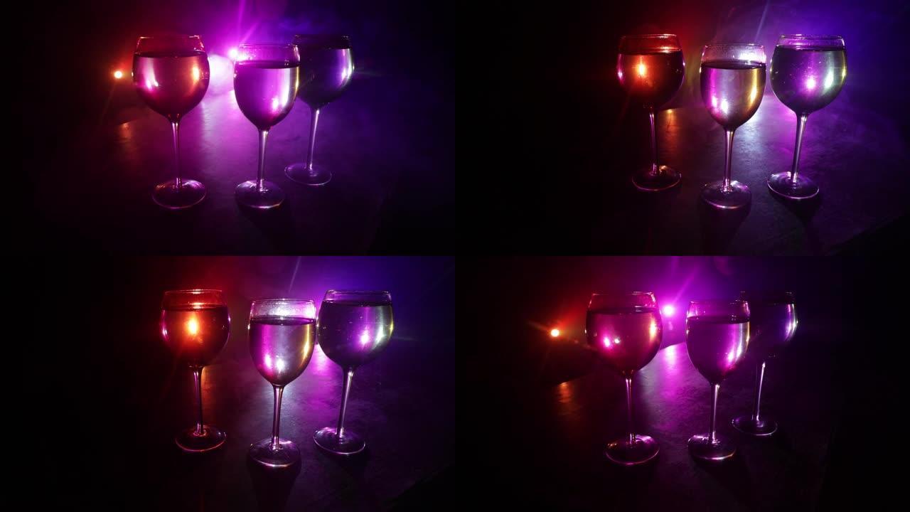 木桌上的酒杯，背景上有美丽的调色灯。深色背景上的一杯葡萄酒。选择性聚焦。俱乐部饮料概念。滑块镜头