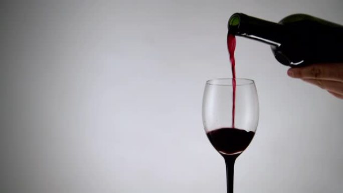 将红酒倒入白色背景的玻璃杯中。淡淡的背景下充满酒精饮料的酒杯