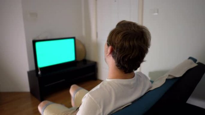 年轻人坐在沙发上看电视时笑的绿色屏幕
