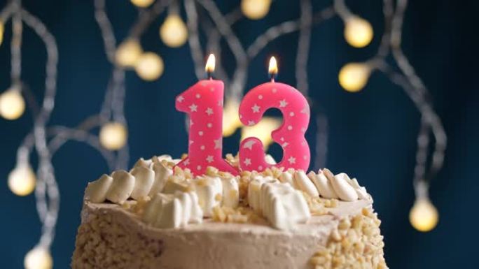 蓝色背景上有13号粉色蜡烛的生日蛋糕。蜡烛吹灭了。慢动作和特写视图