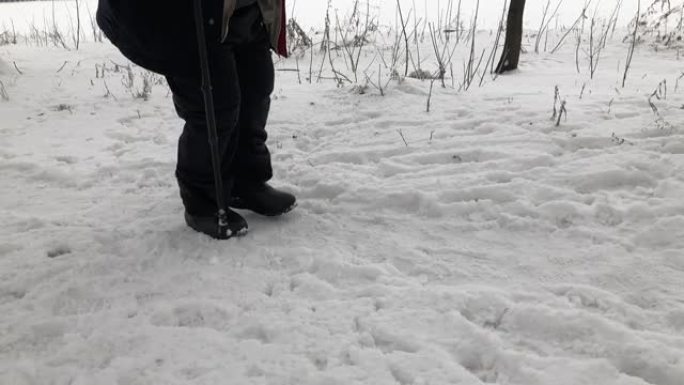 超重的老人用手杖在积雪覆盖的道路上艰难行走