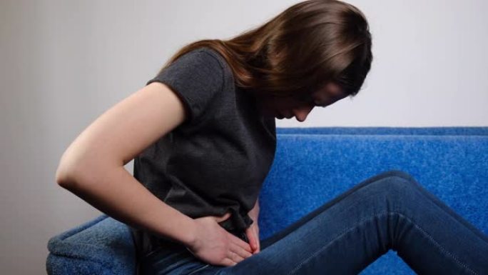 胃痛概念。坐在沙发上的年轻女子的侧视图抱着肚子痛苦感到疼痛不适伤害腹部疼痛有胰腺炎问题，消化不良症状