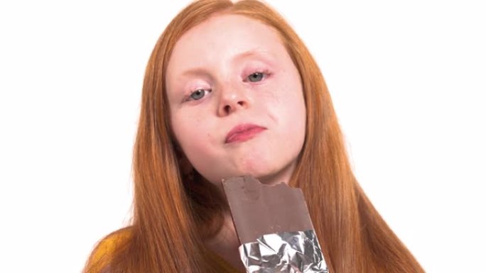 狐狸头发的女孩的特写镜头，绿色的眼睛咬着一块巨大的巧克力。小孩吃甜食