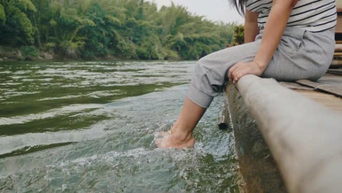 亚洲妇女坐在竹墩上，在河上泡脚。
