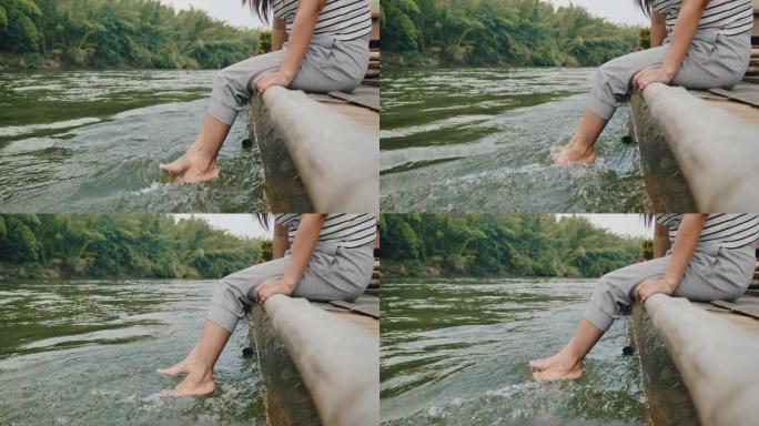 亚洲妇女坐在竹墩上，在河上泡脚。